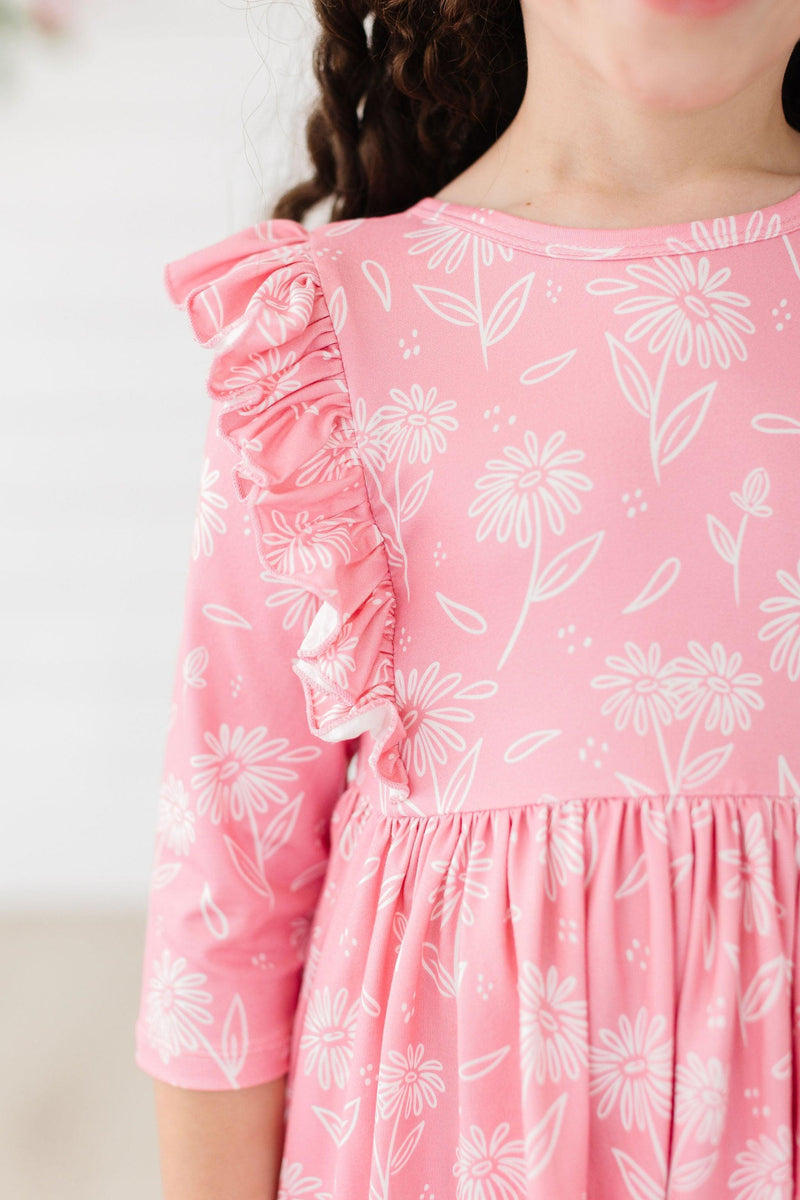 Close-up of a young girl wearing the Dahlia Doodles 3/4 Sleeve Ruffle Twirl Dress in pink with floral patterns, showcasing the ruffled sleeve detail.