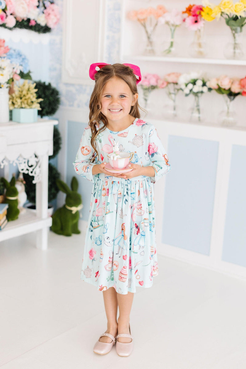 A happy girl standing and holding a decorated tea cup, wearing the Wonderland 3/4 Sleeve Pocket Twirl Dress, capturing the essence of playful elegance.