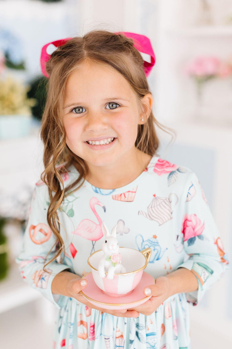 A delighted girl holding a decorative tea cup while wearing the Wonderland 3/4 Sleeve Pocket Twirl Dress with playful designs, embodying a joyful tea party moment.