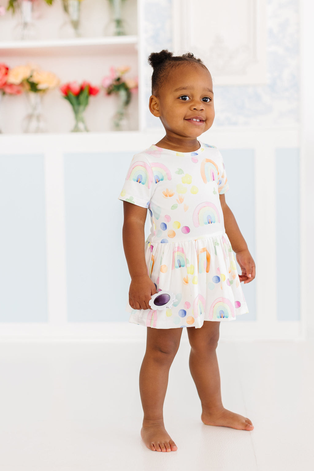 Happy child wearing the Watercolor Rainbows S/S Twirl Bodysuit by Mila & Rose, featuring colorful rainbows and polka dots, perfect for playful adventures and twirling fun.