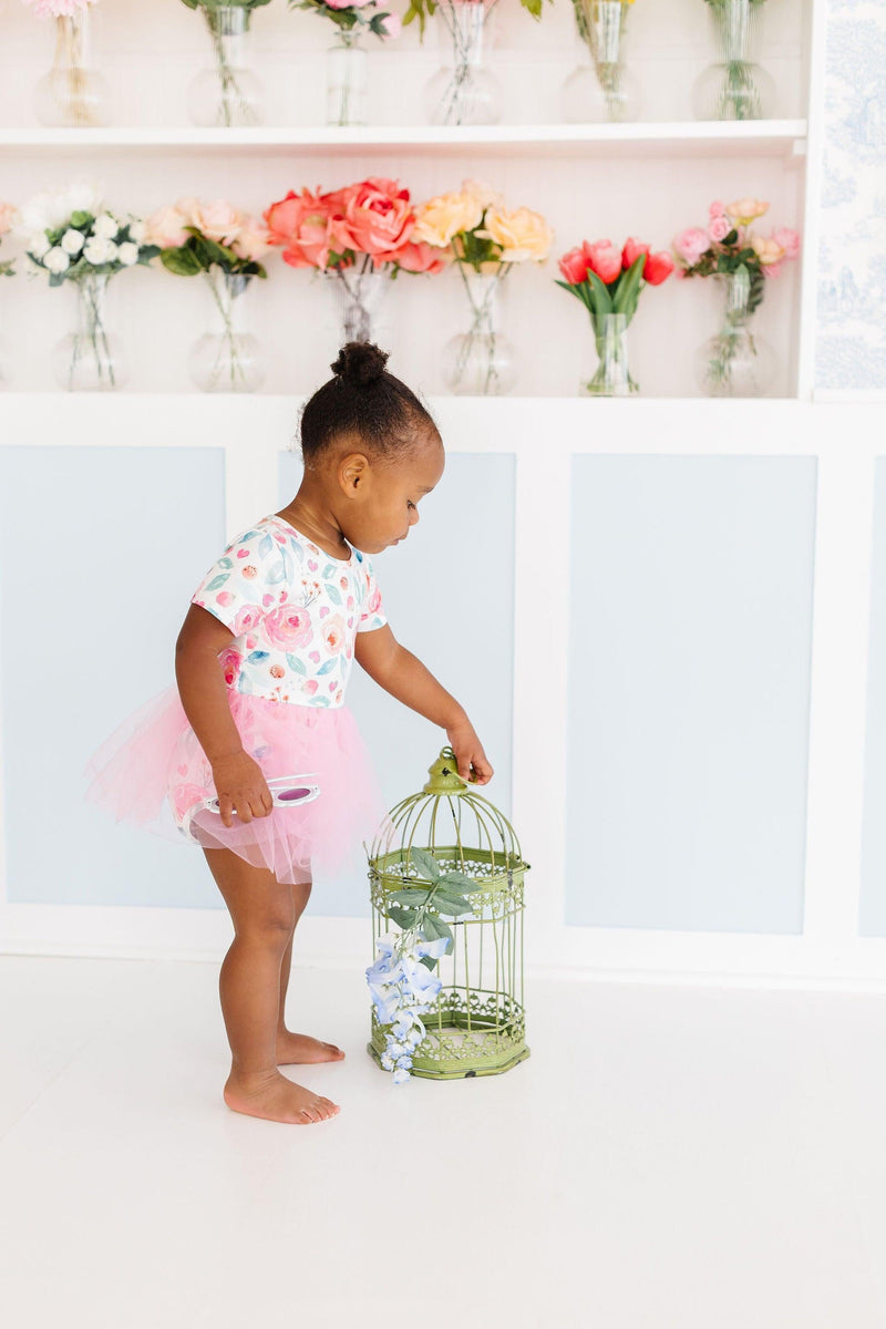 Baby exploring with a birdcage while wearing a SALE Rosettes Pink Tutu Bodysuit for Babies and Toddlers, featuring a vibrant floral pattern.