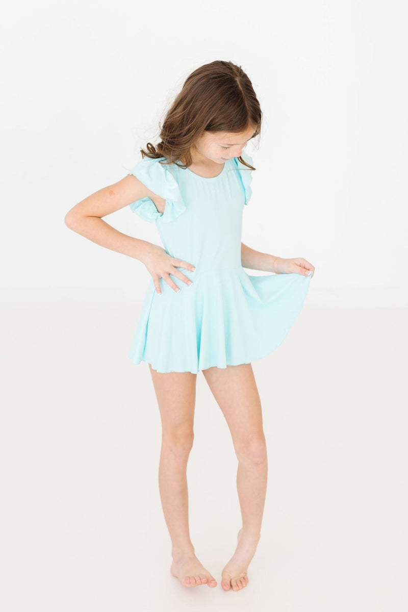 A young girl modeling the Aqua S/S Twirl Leotard from Mila & Rose, featuring a twirl-friendly skirt and stylish flutter sleeves, ideal for dance or play.