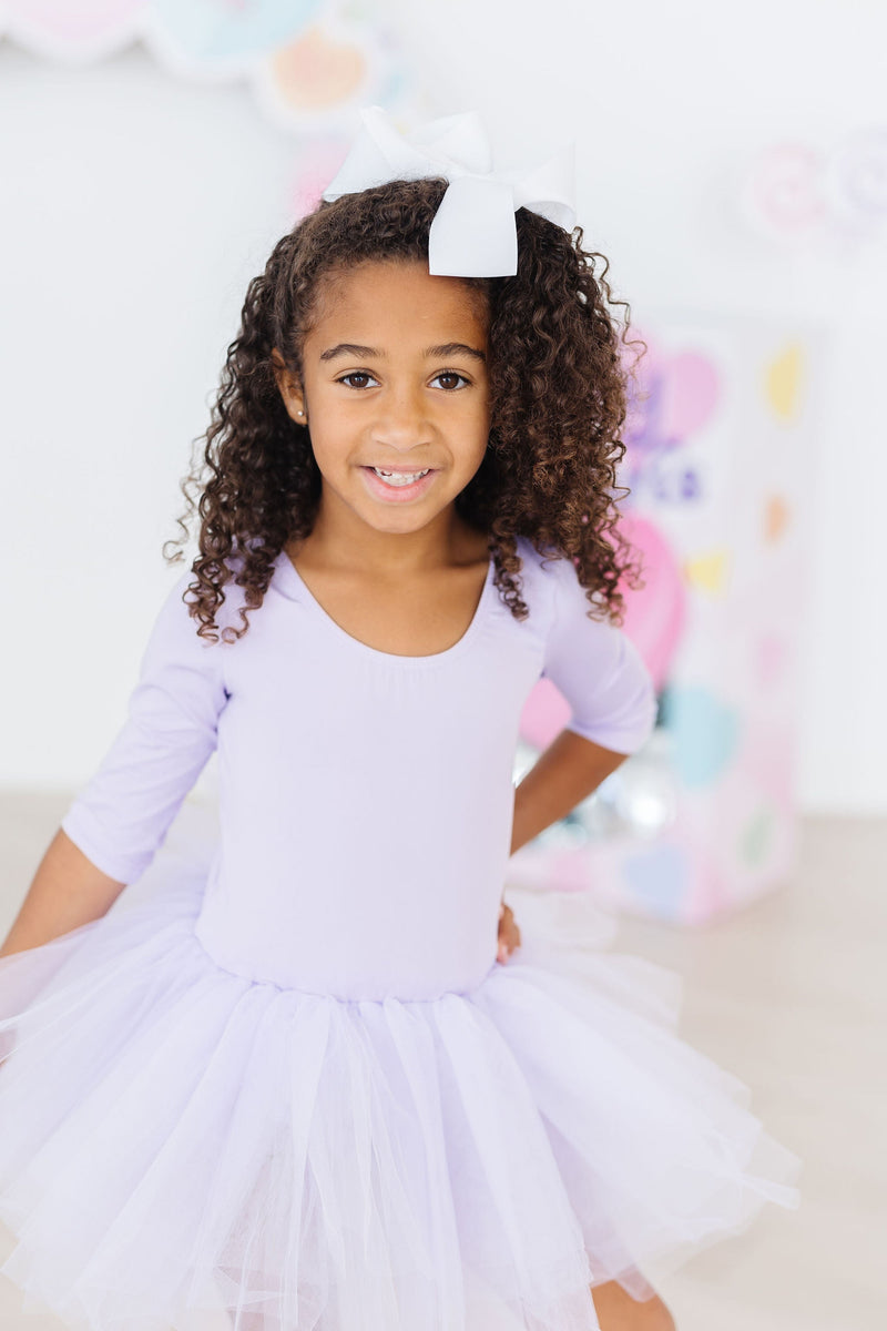 Delighted child in the Lavender 3/4 Tutu Leotard, displaying her fluffy tutu with a confident pose against a colorful backdrop.