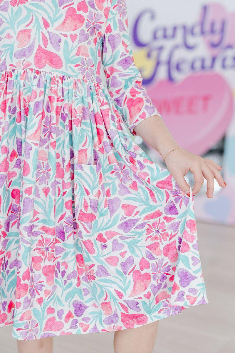 Model wearing the Watercolor Hearts 3/4 Sleeve Pocket Twirl Dress while sitting in a playful pose.