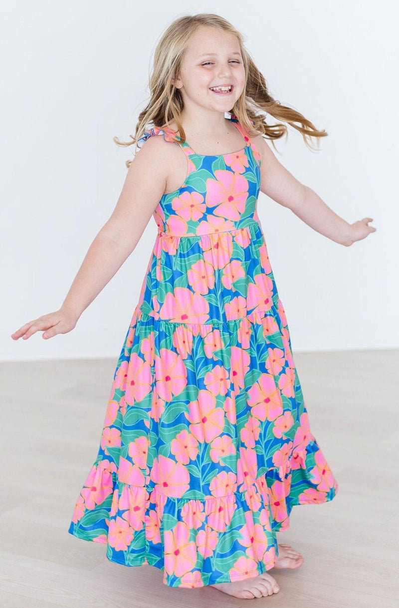 A joyful girl twirls in her Luau Floral Ruffle Maxi Dress, showcasing the colorful floral design and ruffled straps, embodying the spirit of summer fun.