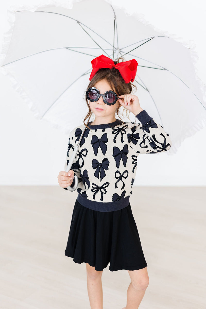 A stylish girl holding an umbrella, wearing a Black Twirl Skort from Mila & Rose, paired with a cute sweater and a bright red bow.
