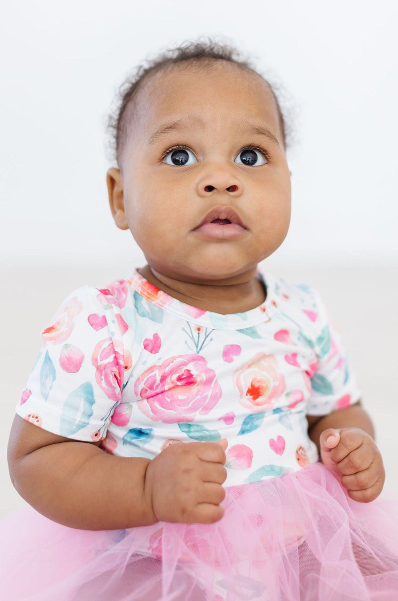 Curious baby girl in a SALE Rosettes Pink Tutu Bodysuit for Babies and Toddlers, showcasing the floral design and whimsical tutu.
