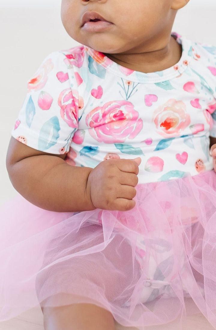 Close-up of a baby wearing a SALE Rosettes Pink Tutu Bodysuit for Babies and Toddlers, showcasing the floral print and fluffy pink tutu.