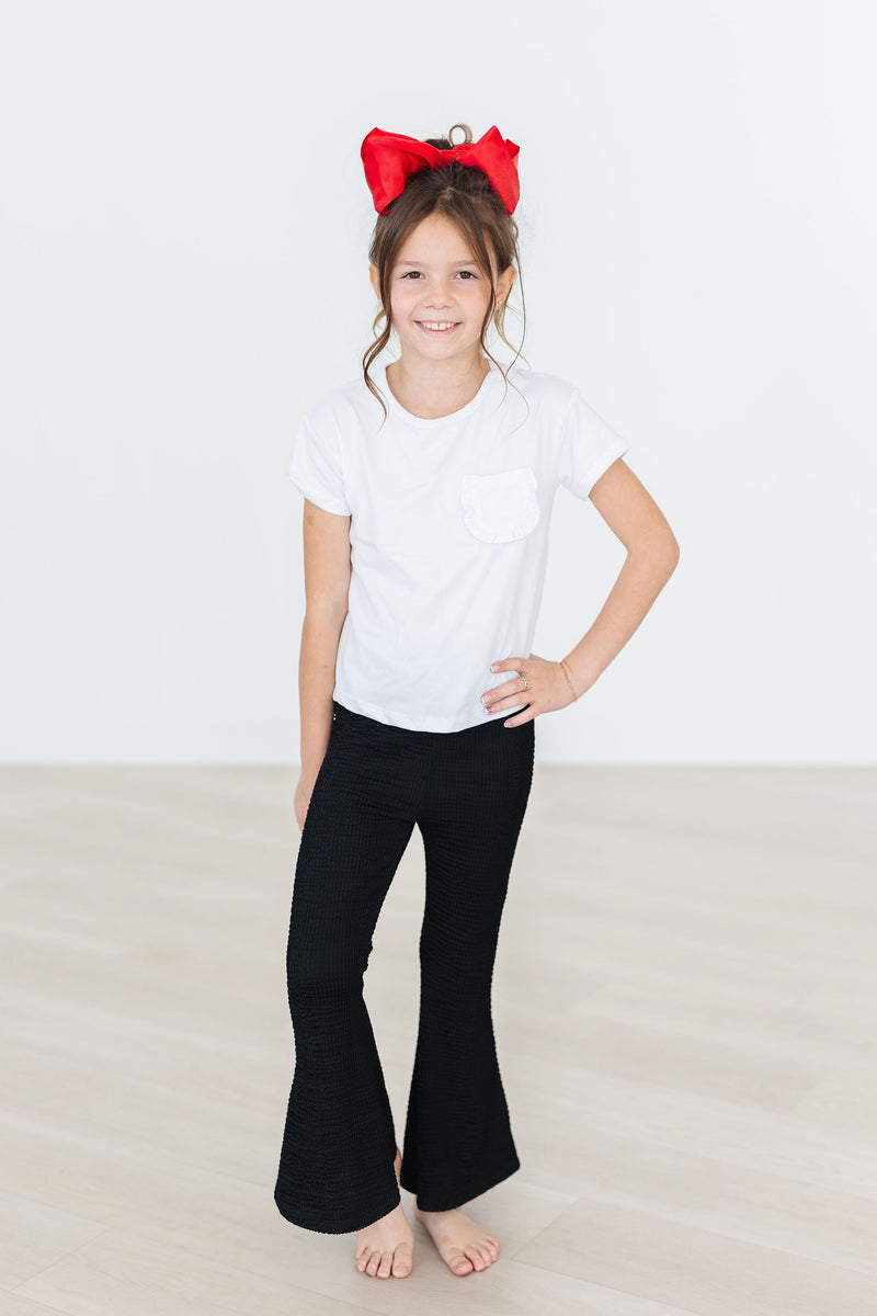 Young girl wearing Black Scrunchy Bells paired with a white top and a playful red bow, embodying a trendy style suitable for any occasion.