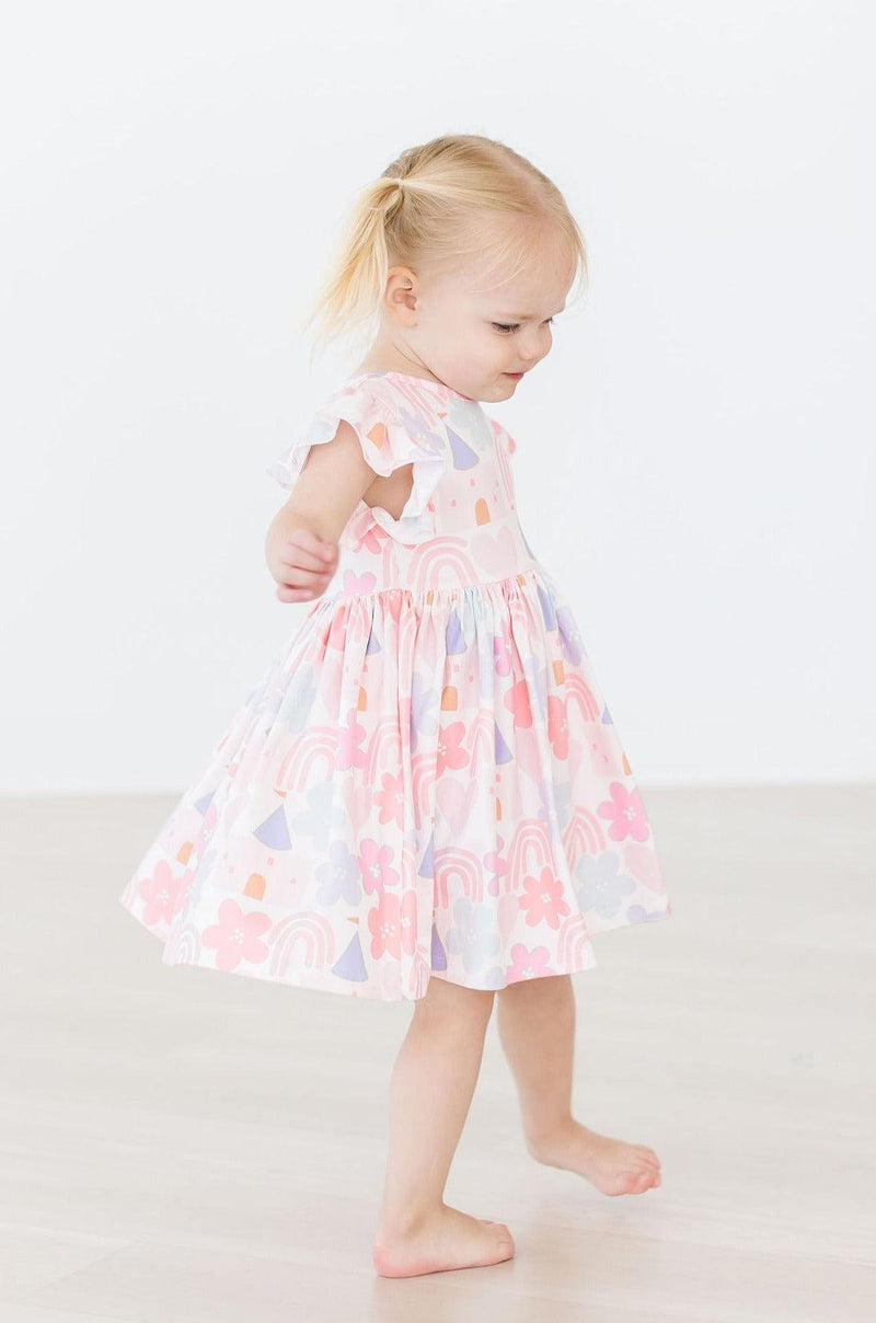 Stylish girl wearing the Castles & Rainbows Flutter Sleeve Twirl Dress, demonstrating its comfortable fit and enchanting design.