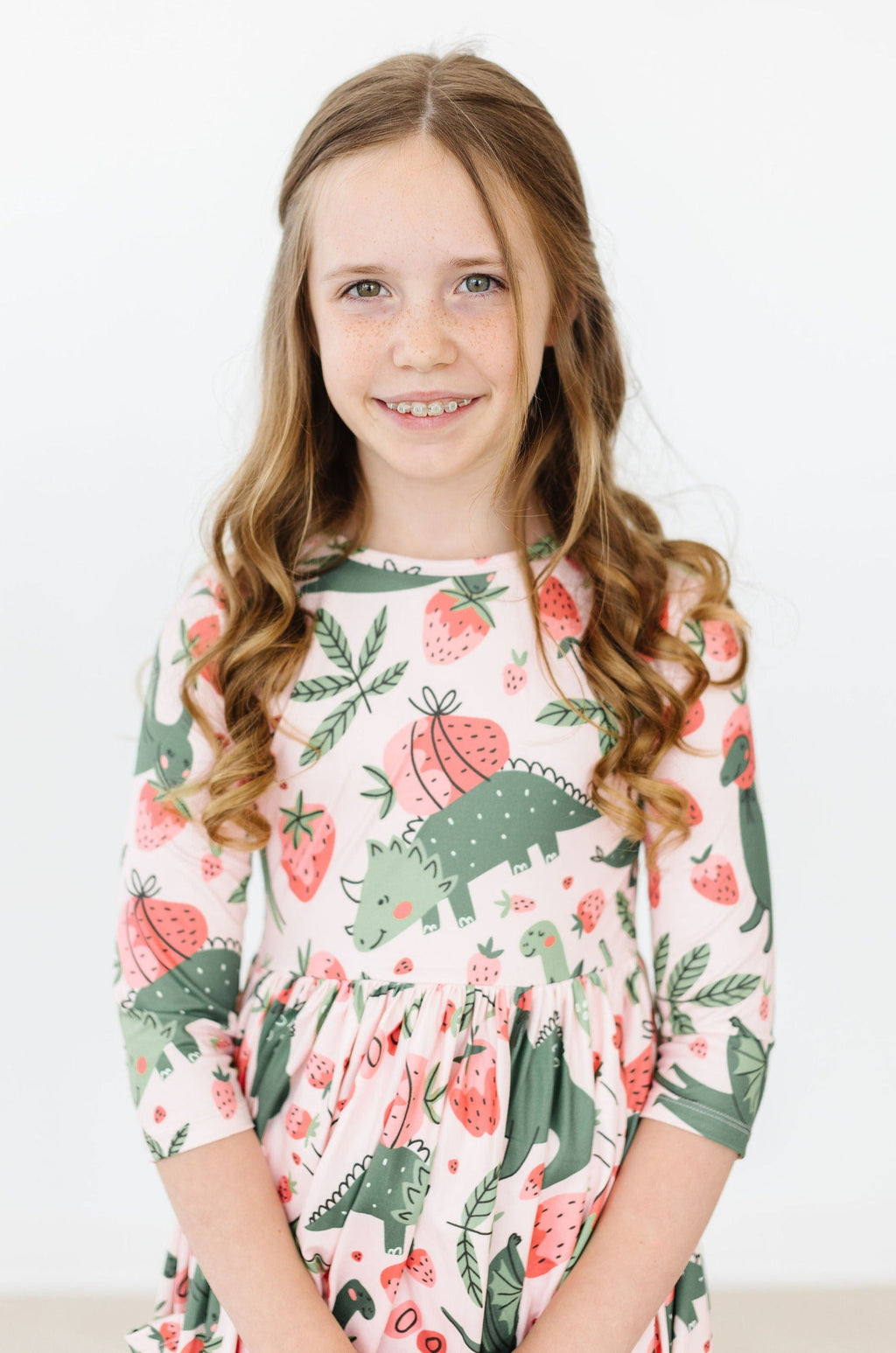 'Hear Me Roar' 3/4 Sleeve Pocket Twirl Dress for Girls modeled by a smiling girl with long curls, featuring a playful dinosaur and strawberry pattern.