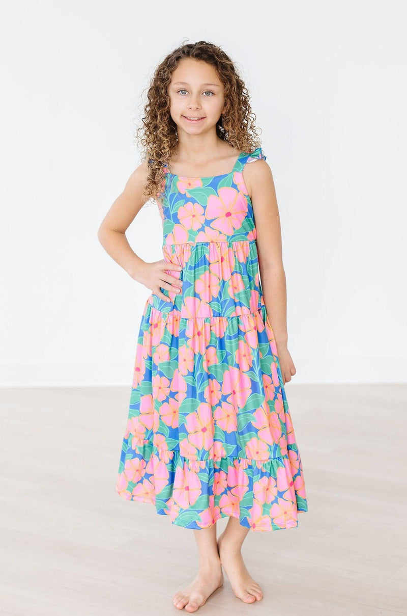 A confident young girl poses in the Luau Floral Ruffle Maxi Dress, highlighting the stunning floral print and comfortable fit, perfect for any sunny outing.