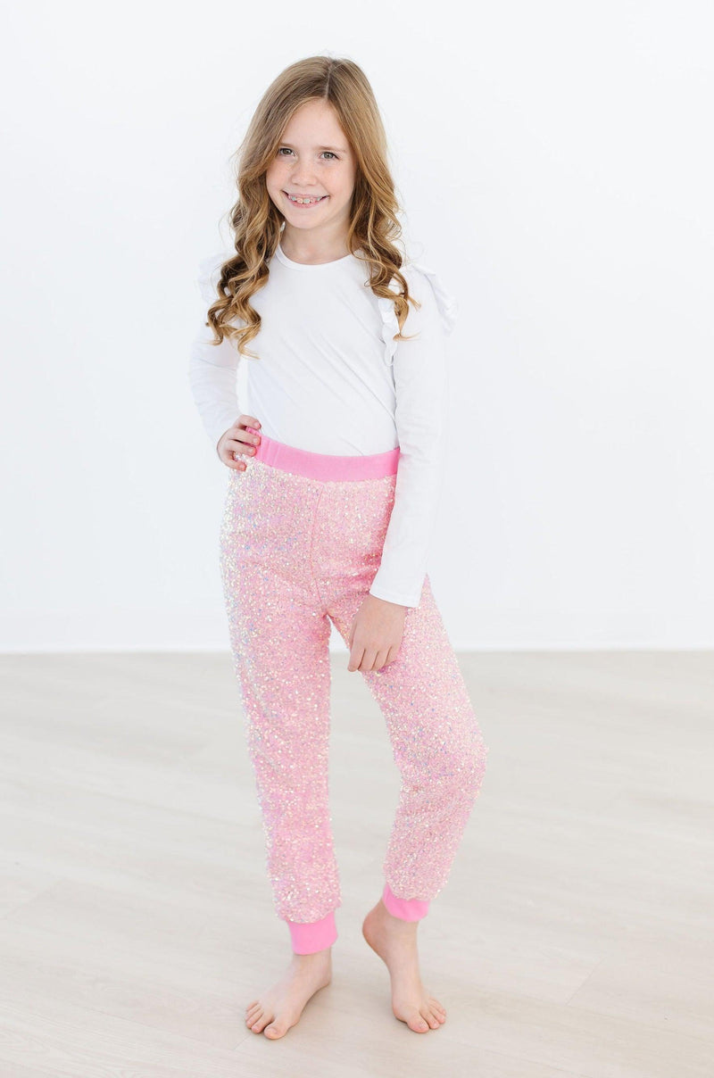 A girl modeling Bubblegum Pink Sequin Joggers by Mila & Rose ®, paired with a white top, highlighting the stylish sequined design and comfortable fit ideal for celebrations.