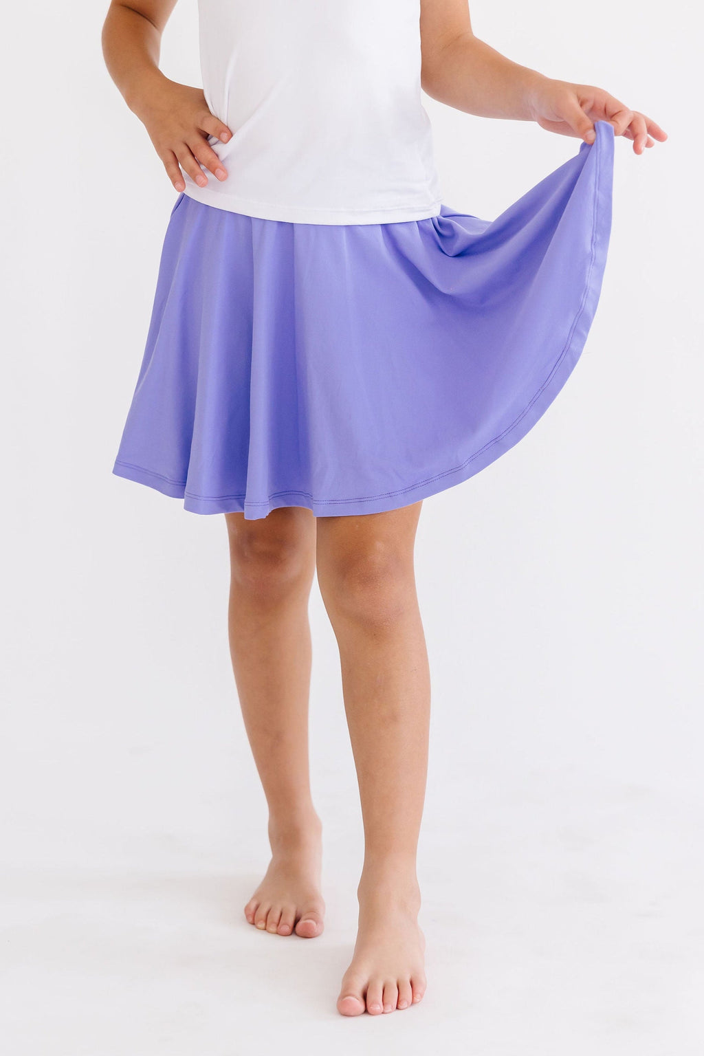 A young girl showcasing the Periwinkle Twirl Skort from Mila & Rose®, twirling playfully with a smile, highlighting its flowy design and chic light blue color.