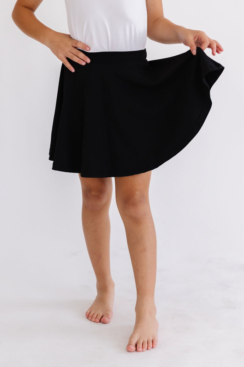A young girl showcasing the flow of the Black Twirl Skort from Mila & Rose, spinning gracefully while wearing a white top.
