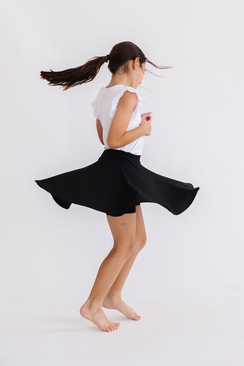 A playful moment of a girl in the Black Twirl Skort from Mila & Rose, spinning joyfully, showcasing the comfort and style of the skort.