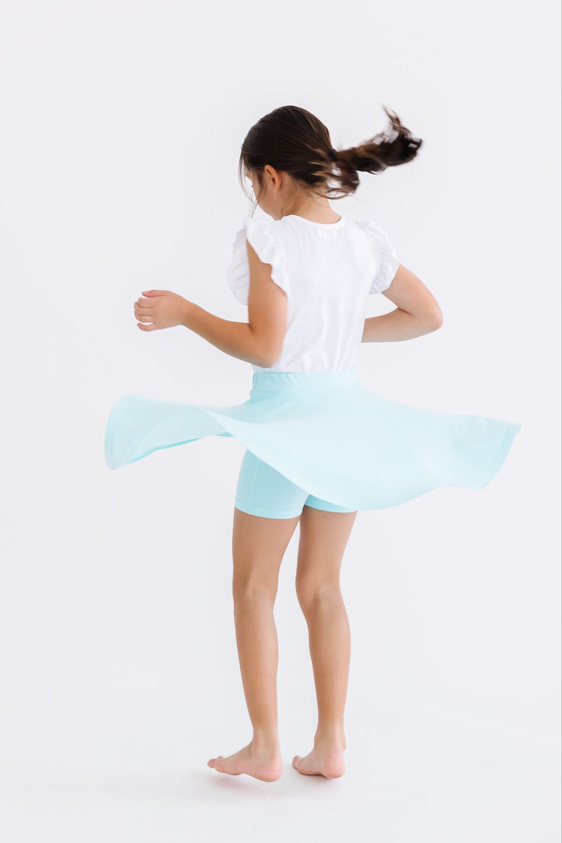 A girl spins joyfully while wearing the Aqua Twirl Skort by Mila & Rose®, highlighting the skort's twirl feature with attached shorts.