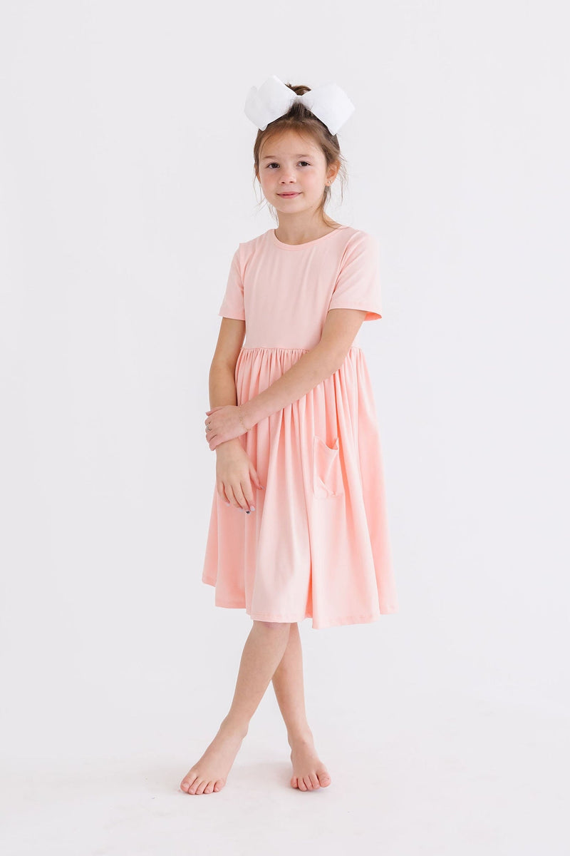 Adorable child posing in the Peach S/S Pocket Twirl Dress by Mila & Rose, highlighting the dress's twirl-friendly style and soft fabric.