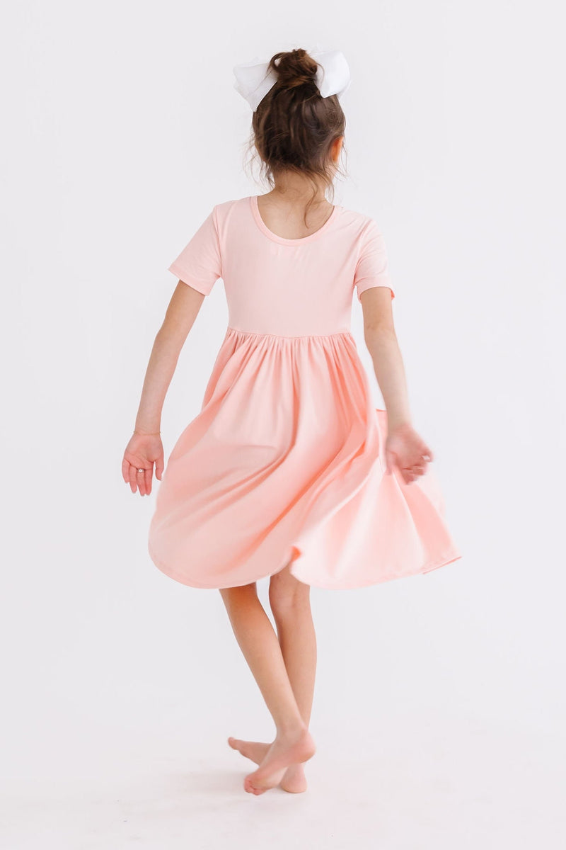 Back view of a girl spinning in the Peach S/S Pocket Twirl Dress by Mila & Rose, emphasizing the dress's twirling feature and comfortable fit.