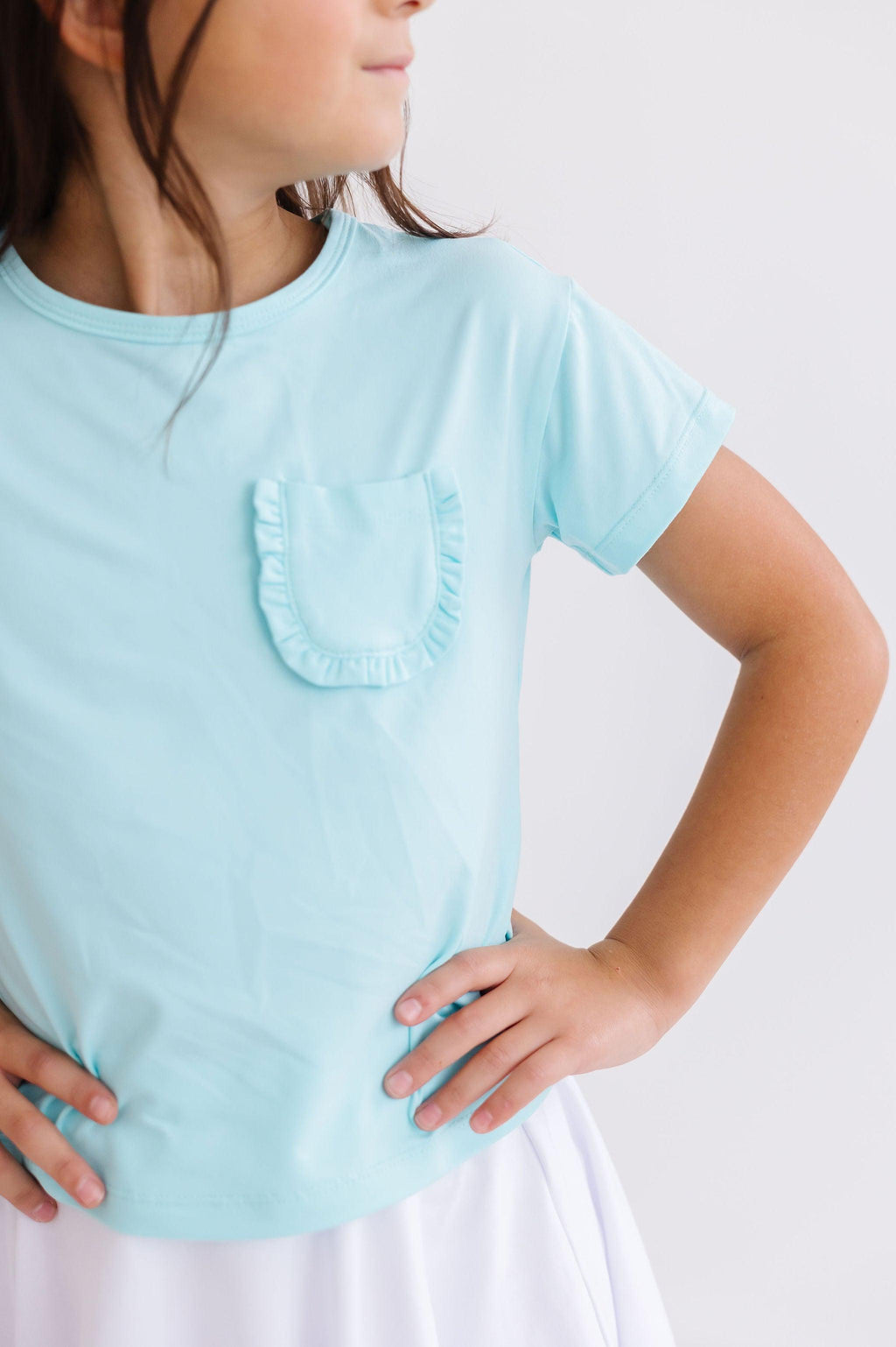Aqua Ruffle Pocket Tee from Mila & Rose, showcasing a stylish young girl with hands on her hips, confidently modeling the trendy top with a ruffled pocket, perfect for playful days.