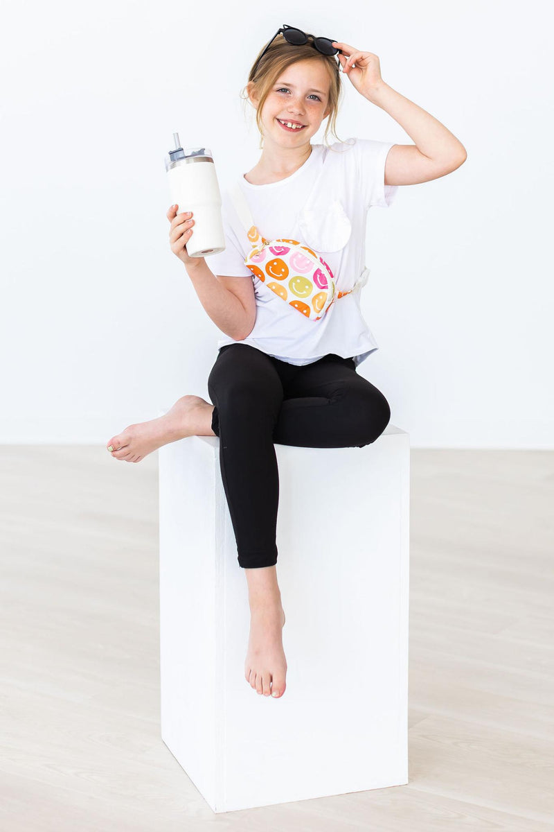 Young girl enjoying a fun day with Comfy-Fit Black Leggings for Girls, sipping a drink and posing with a playful smile, styled with a casual white tee.