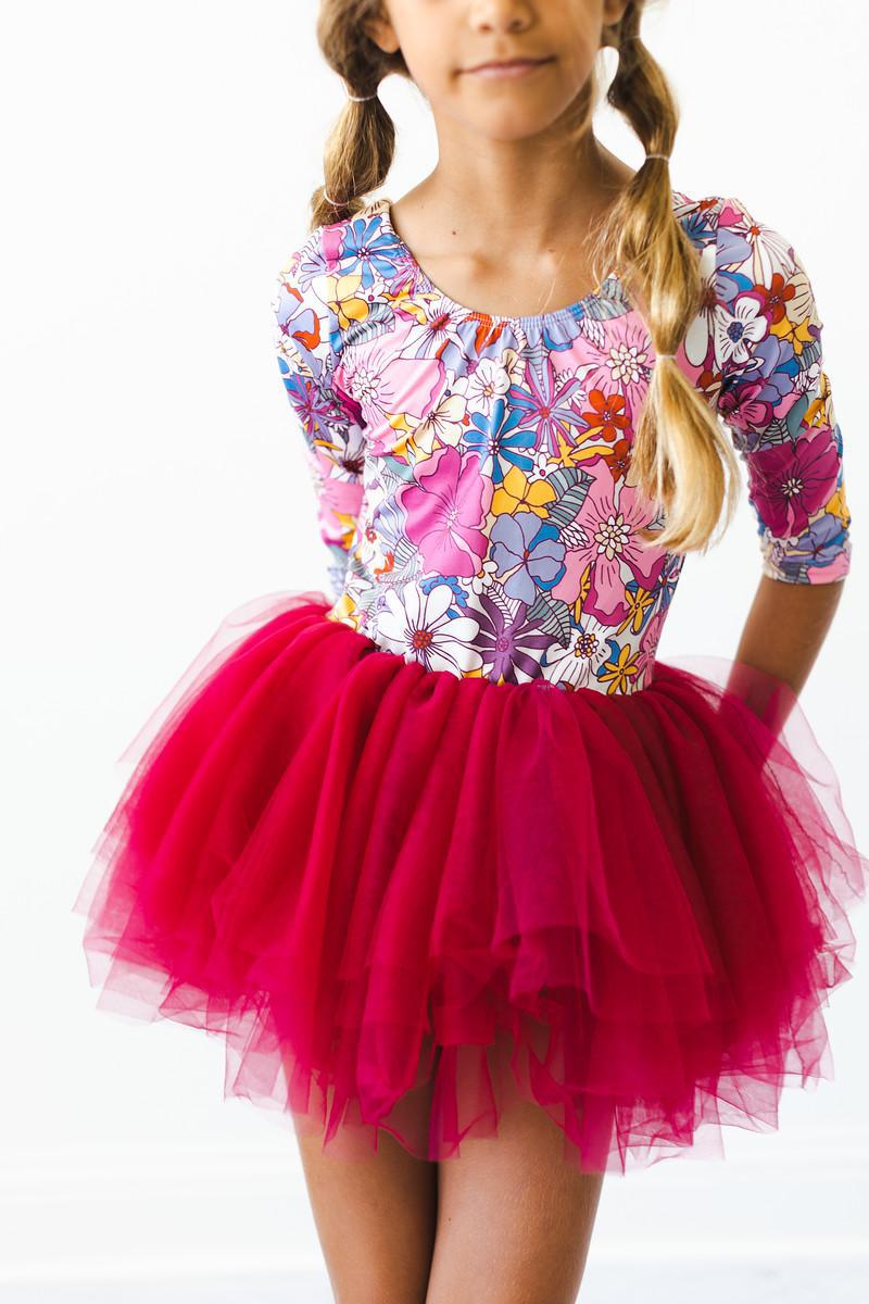 Young girl showcasing the Mauve What's Up Buttercup 3/4 Tutu Leotard with a floral print, paired with a fluffy tulle skirt, perfect for dance classes and playful moments.