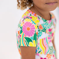 The Second-Skin 2-Piece Short Sleeve Pajama in Rainbow Daisy Babe worn by a child in a bright floral print.