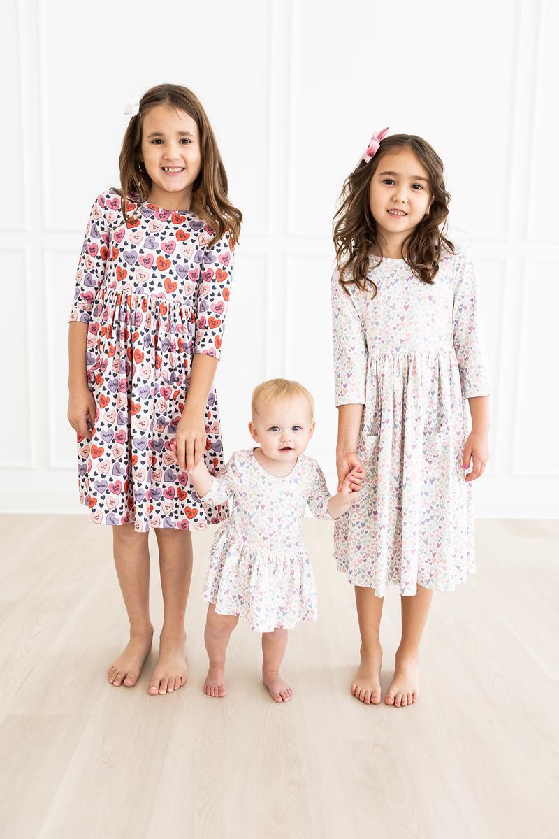 Three girls, including a toddler in the One in a Million 3/4 Sleeve Twirl Bodysuit by Mila & Rose®, posing together in matching dresses for a cute family photo.
