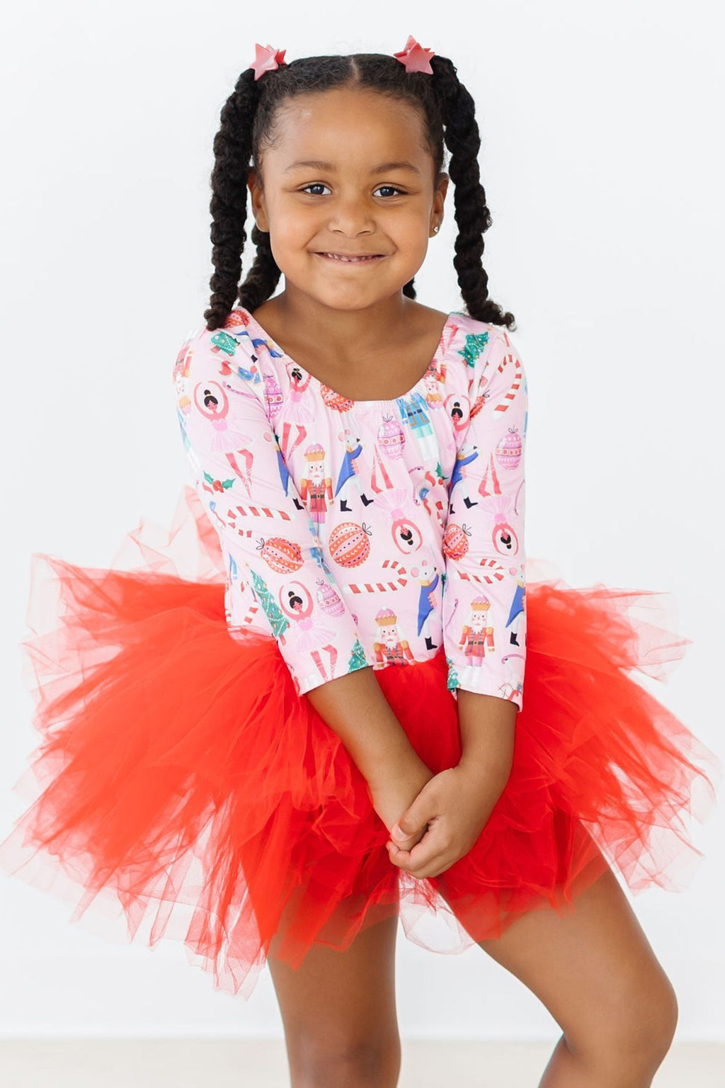 Happy child wearing the Sugarplum Fairy 3/4 Tutu Leotard by Mila & Rose®, featuring a colorful festive print and a fluffy red tutu, perfect for dance classes or play.