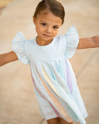Little girl twirling in a light blue swing dress with flutter sleeves and colorful rainbow pleats across the front.