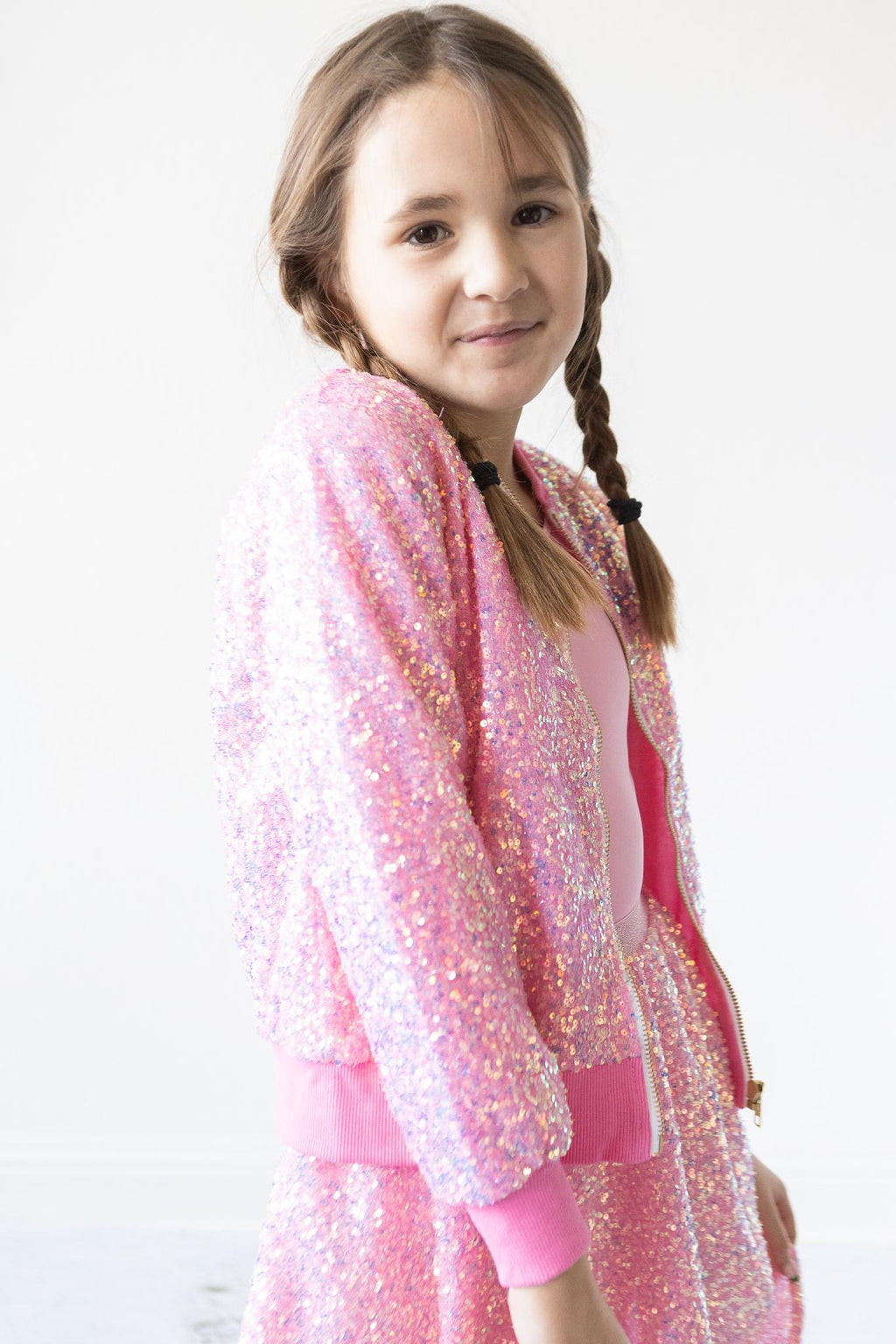 Girl wearing a Bubblegum Pink Sequin Jacket, smiling with braided hair, showcasing a sparkly and stylish look.