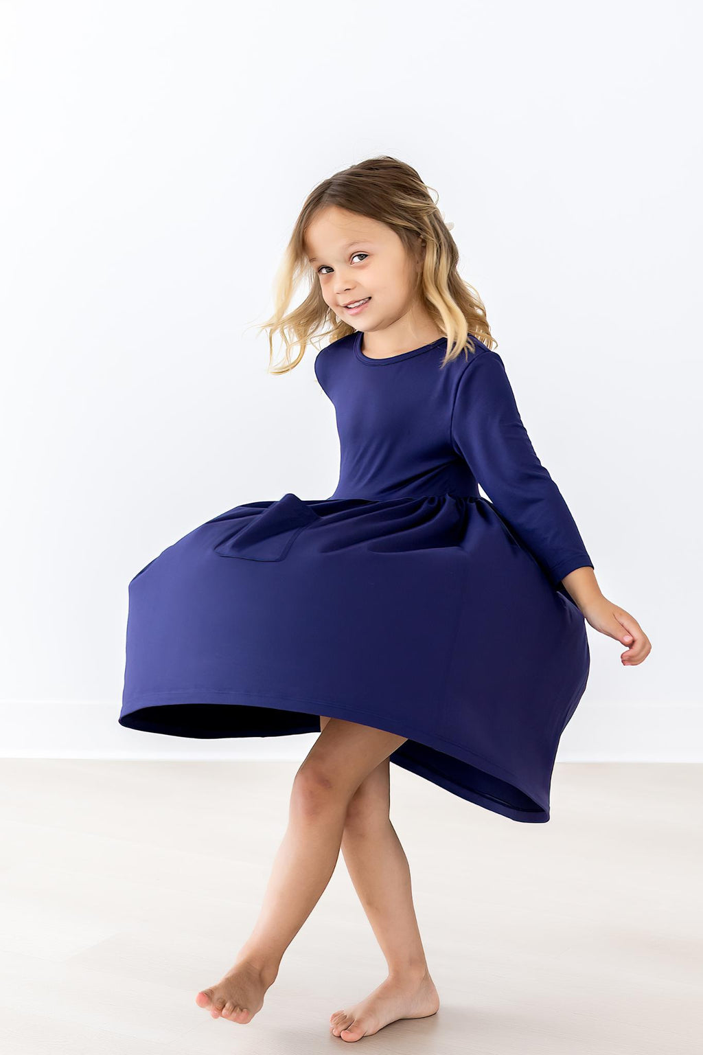 A cheerful child wearing a Navy 3/4 Sleeve Pocket Twirl Dress by Mila & Rose, playfully twirling and showcasing the dress's charming design and elegant fit.