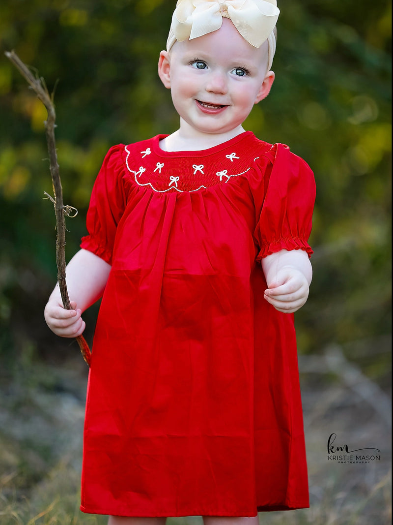 Little girl in red dress with smocked embroidery and bow accents outdoors