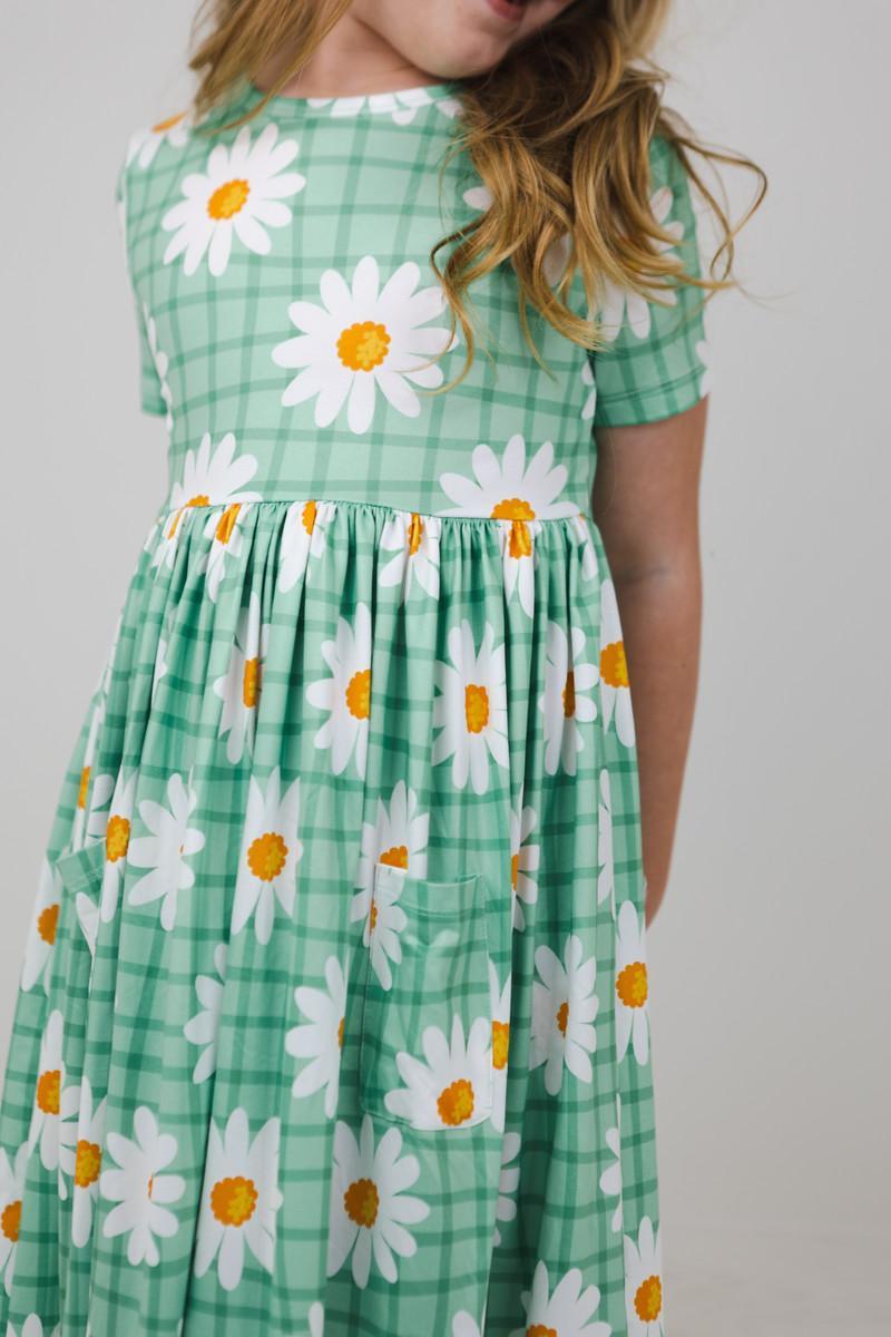 Charming Off the Grid S/S Pocket Twirl Dress featuring vibrant green plaid with daisy patterns, perfect for twirls and playdates.