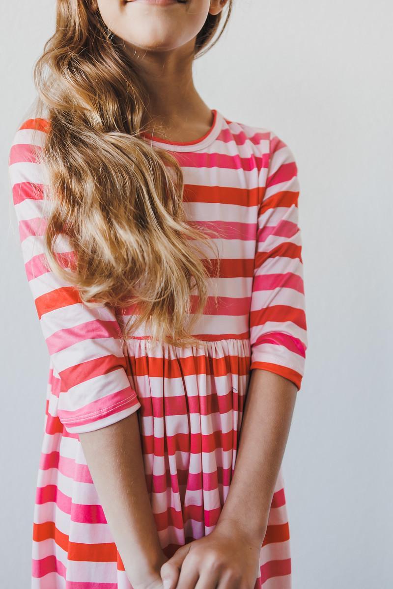 Stylish portrait of a girl in the All You Need is Love 3/4 Sleeve Pocket Twirl Dress with pink and orange stripes, making it an adorable twirl dress for girls.