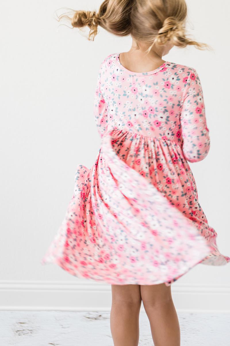 A young girl twirling in the Azalea 3/4 Sleeve Pocket Twirl Dress by Mila & Rose, featuring a floral pattern. This charming dress combines style and comfort, perfect for playtime or special occasions.