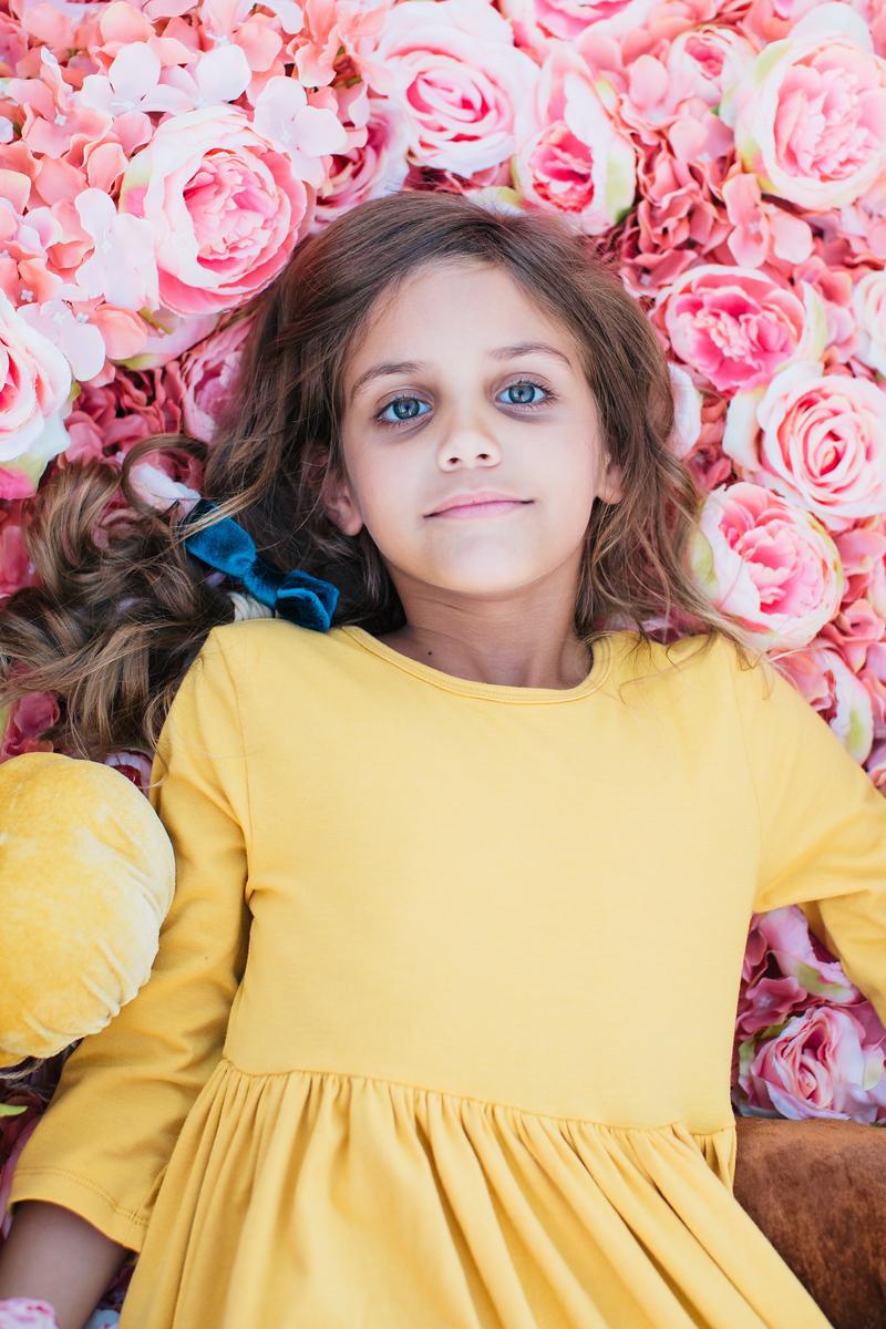 Close-up of a girl resting among pink roses, wearing the Mustard 3/4 Sleeve Pocket Twirl Dress by Mila & Rose®, emphasizing the dress's comfort and style.