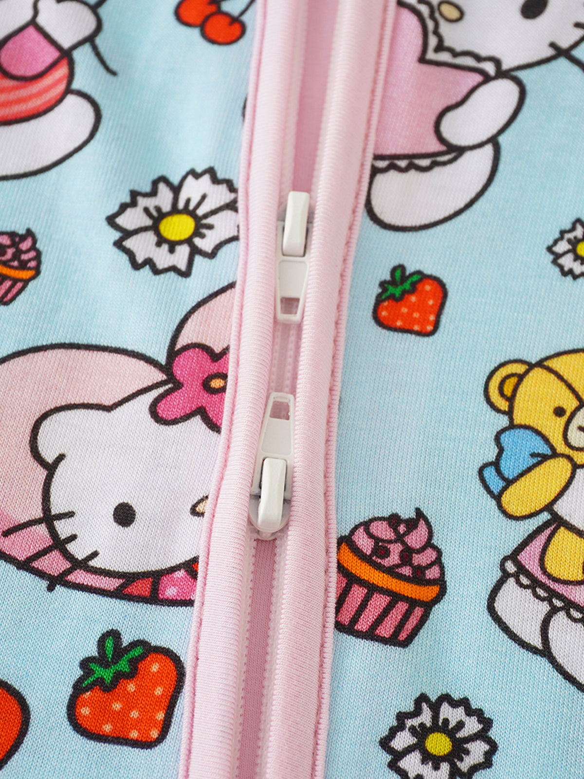 Dual white plastic zipper pulls on pink tape against light blue Hello Kitty and strawberry print