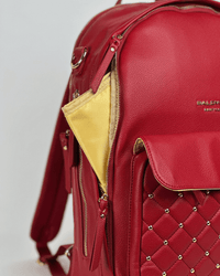 Crimson vegan leather diaper bag featuring gold studs, quilted detailing, and a glimpse of yellow interior lining.