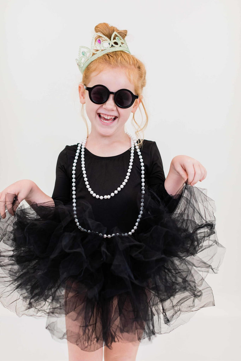 Cheerful girl in a Black 3/4 Tutu Leotard, wearing stylish sunglasses and a tiara, striking a fun pose with a beaded necklace.
