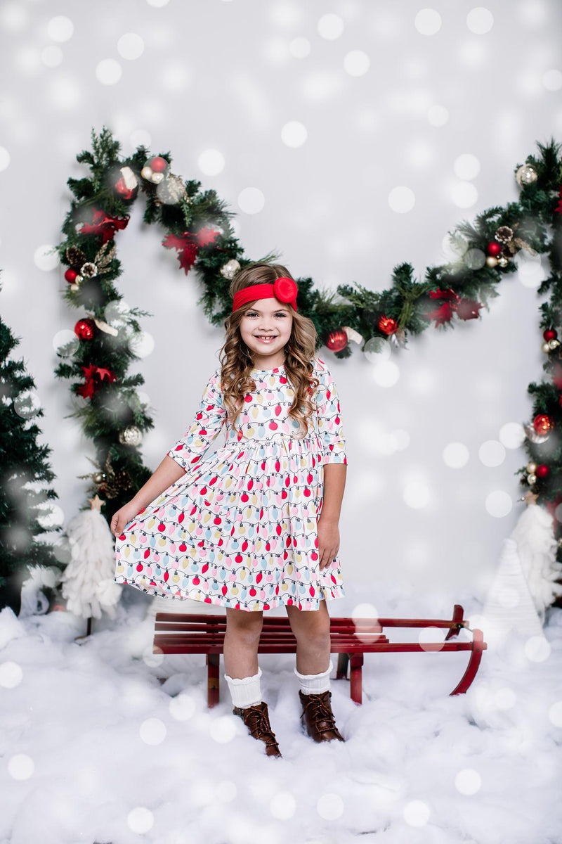Young girl wearing the Merry & Bright 3/4 Sleeve Pocket Twirl Dress by Mila & Rose®, set against a festive background with garlands and snow, radiating holiday cheer.