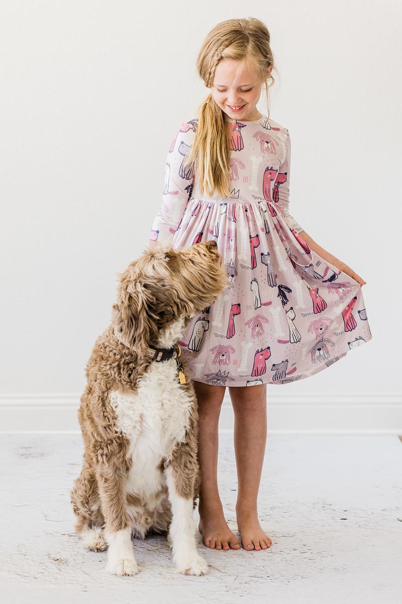 A girl wearing the Adorable Puppy Party 3/4 Sleeve Girls Pocket Twirl Dress, smiling with her dog beside her, showcasing the playful design.