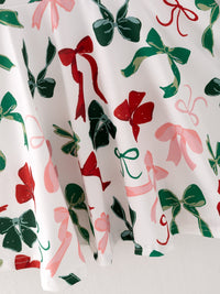 Festive white girls dress fabric featuring red, green, and pink bow prints for a cute holiday look.