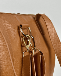 Macro shot of gold-tone D-rings and swivel snap hooks connecting shoulder strap to textured cognac leather body