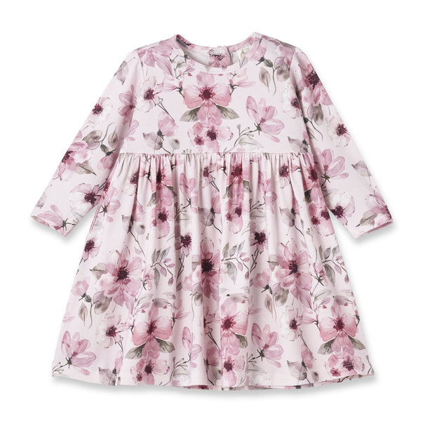 A long-sleeve children's dress with a pink and purple watercolor floral print on a light pink background, featuring a gathered waist seam.