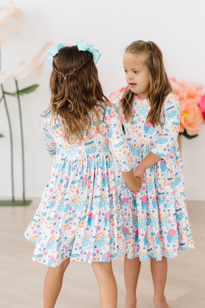 Two happy friends holding hands in their matching Egg-cellent 3/4 Sleeve Pocket Twirl Dresses by Mila & Rose, featuring vibrant patterns and a comfortable fit for endless twirling fun.