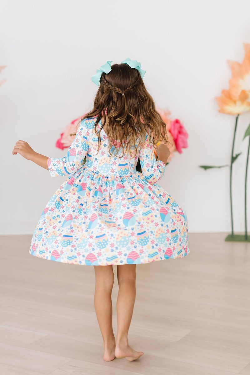 A joyful child twirling in the Egg-cellent 3/4 Sleeve Pocket Twirl Dress by Mila & Rose, showcasing a colorful floral design and playful skirt perfect for any occasion.