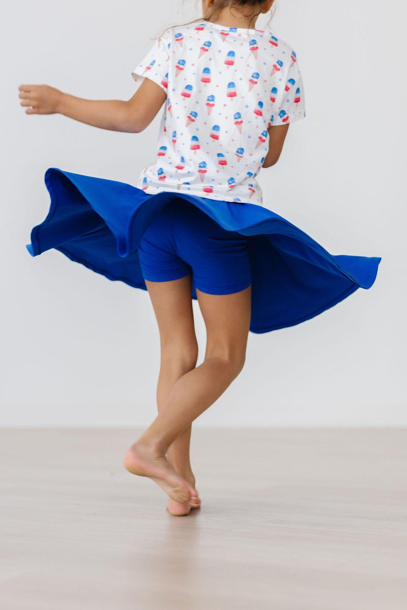 A child wearing the Royal Blue Twirl Skort from Mila & Rose, spinning around with a vibrant blue skort in action, showcasing built-in shorts.