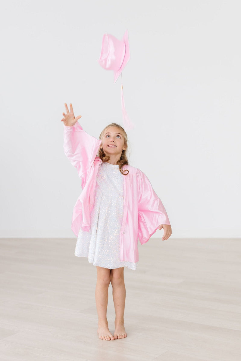 A girl throwing her pink graduation cap in the air, wearing a white sequin party dress, capturing a moment of excitement and fun.