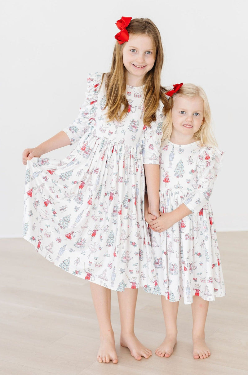 Two adorable girls wearing Clara's Christmas 3/4 Sleeve Ruffle Twirl Dresses in a coordinated holiday print, showcasing the dresses' twirling and playful style.